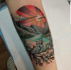 a person with a tattoo on their arm that has mountains and trees in the background