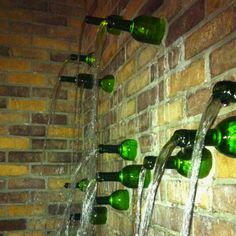 several green wine bottles are lined up on the wall with water coming out of them