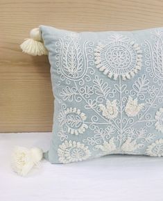 a decorative pillow with tassels on top of it sitting on a white bed