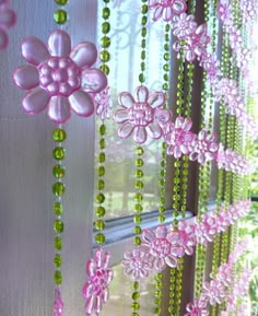 pink and green beaded curtains hanging from a window sill with flowers on them