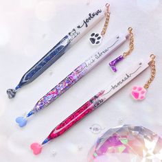 three pens are laying next to each other on a white surface with jewels around them