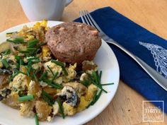 a white plate topped with an egg salad next to a muffin on top of a blue napkin