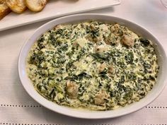 a white bowl filled with spinach and cheese on top of a table next to bread