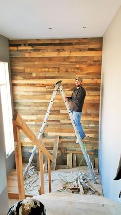 a man standing on a ladder in front of a wooden wall with wood planks