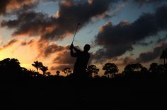 the silhouette of a man holding a golf club at sunset