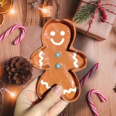 a hand holding a ginger cookie on top of a wooden table next to christmas decorations