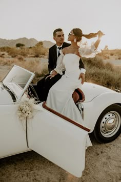 a bride and groom sitting on the back of a white convertible car in the desert