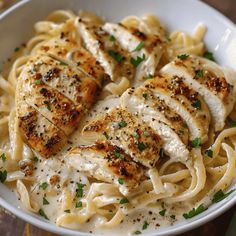 a white bowl filled with pasta and chicken covered in parmesan cheese sauce on top of a wooden table