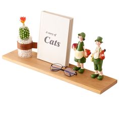 two figurines are standing on a shelf next to a book and some cacti