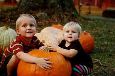 two young boys sitting on pumpkins in the grass