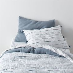 an unmade bed with blue and white comforter on the bottom, along with two pillows