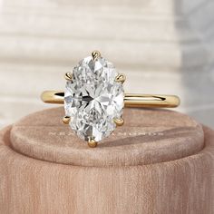 an oval cut diamond sits on top of a wooden ring box in front of a white marble wall