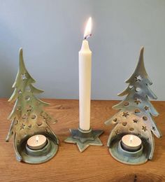 two candles are sitting next to each other with christmas trees in the middle and one candle is lit