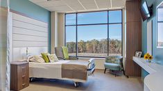 a hospital room with a large window and a bed in the middle, along with two chairs