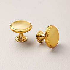 a pair of gold cabinet knobs on a white surface