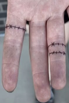 two fingers with barbed wire tattoos on each one's thumb and the middle finger