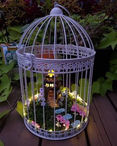 a white birdcage filled with flowers and fairy lights on top of a wooden table