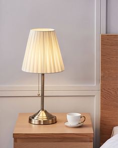 a lamp on a nightstand next to a cup and saucer