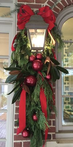 a christmas wreath hanging on the side of a building with red balls and greenery