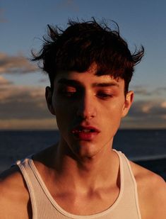 a young man standing in front of the ocean with his eyes closed and one eye open