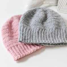 two knitted hats sitting next to each other on top of a white countertop