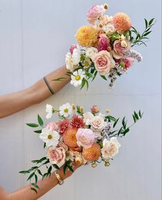 two hands holding bouquets of flowers against a white wall