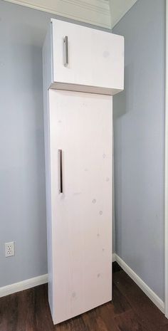 a white refrigerator sitting in the corner of a room next to a wooden floor and wall