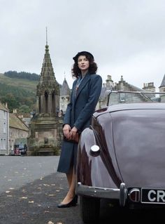 a woman standing next to an old car in front of a church with a steeple