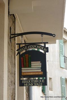 a sign hanging from the side of a building with books stacked on top of it