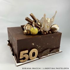 a piece of chocolate cake with gold decorations on top and the number 50 spelled out