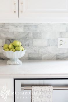 a white bowl filled with green apples on top of a counter