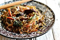 a plate filled with noodles and vegetables on top of a wooden table next to chopsticks