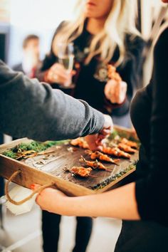 two women are serving themselves food at a party or social gathering, while another woman is holding a wine glass in her hand