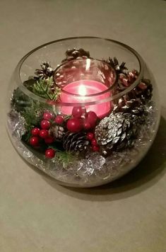 a glass bowl filled with pine cones, holly berries and a lit candle