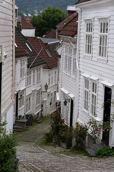 an old cobblestone street with white houses and flowers on the sidewalk in front of them