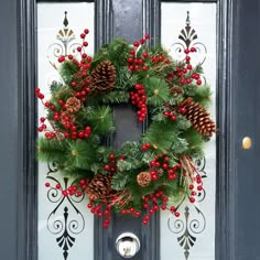 a christmas wreath hanging on the front door with red berries and pineconis around it