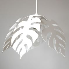 a white light hanging from a ceiling with a large leaf on it's side