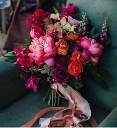 a bouquet of flowers sitting on top of a green couch next to a brown ribbon