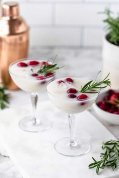 two martinis with cherries and rosemary garnish on a marble countertop