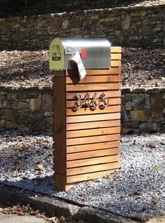 a wooden mailbox sitting on the side of a road next to a stone wall