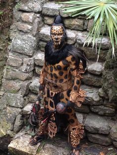 a statue is sitting on some rocks near a plant and stone wall with plants in the background