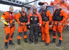 five men in orange jumps standing next to a helicopter