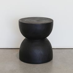 a small black stool sitting on top of a cement floor next to a white wall