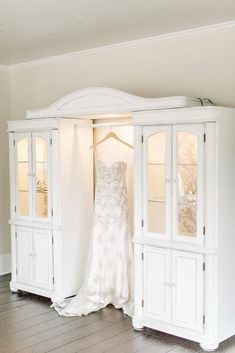 a wedding dress hanging on a white china cabinet