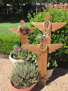 a wooden cross sitting next to a potted planter filled with flowers and greenery