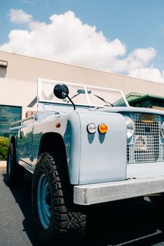 an old blue truck parked in front of a building with a sky background and clouds