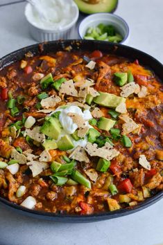 a skillet filled with chili, avocado and tortilla chips on top of a table