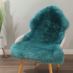 a blue chair with wooden legs in front of a white wall and potted plant