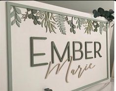 a sign that says ember marie hanging from the side of a wall with leaves on it