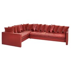 a red leather sectional sofa with lots of pillows on the top and bottom corner, in front of a white background